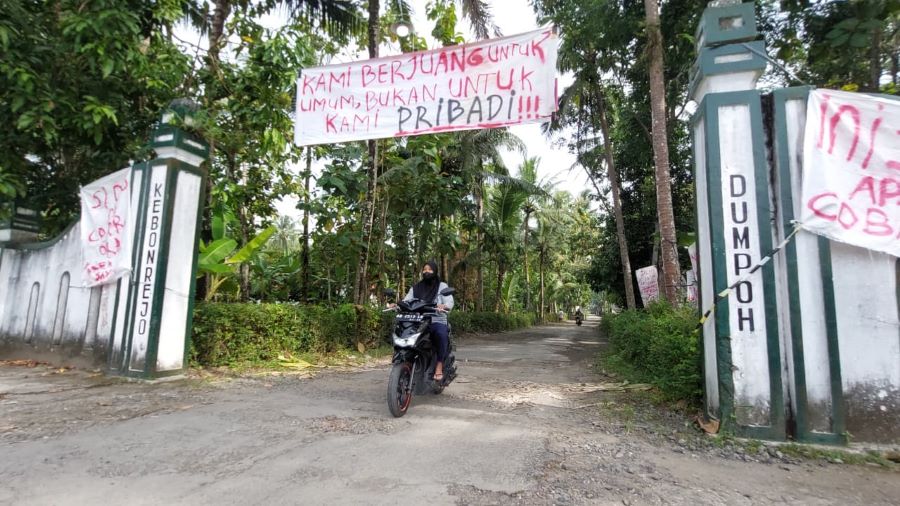 PROTES: Warga Padukuhan Dempoh melewati jalan rusak yang telah ditempeli spanduk.
