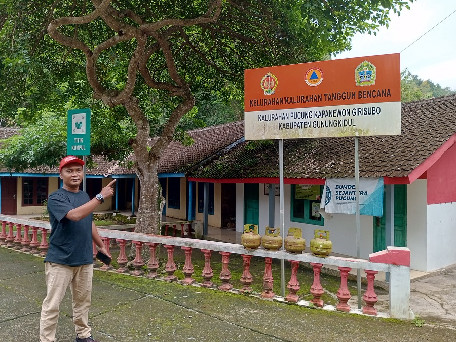 Salah satu warga Pucung sedang menunjukkan papan bertuliskan Kalurahan Tangguh Bencana di Kalurahan Pucung pada Jumat (30/1/2026).
