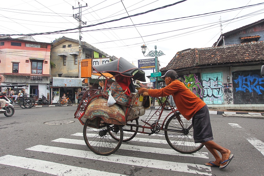 Pengayuh becak mengantarkan penumpang saat melintas di simpang empat Kauman, Kota Jogja, Senin (9/2/2026).
