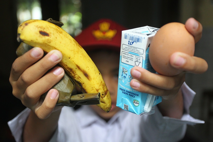 Siswa sekolah dasar menunjukkan menu Makan Bergizi Gratis (MBG) edisi Ramadan untuk dibawa pulang berupa arem-arem, pisang, susu kemasan, dan telur rebus, di Kota Jogja, Senin (23/2/2026).