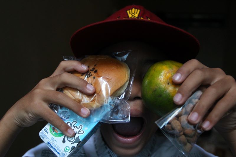 Siswa sekolah dasar menunjukkan menu Makan Bergizi Gratis (MBG) edisi Ramadan untuk dibawa pulang berupa roti, susu kemasan, jeruk, dan kacang telur, di Kota Jogja. 