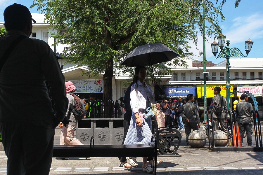 Wisatawan menggunakan payung untuk melindungi diri dari sengatan sinar matahari saat cuaca panas di kawasan Malioboro, Kota Jogja, Selasa (17/3/2026). 