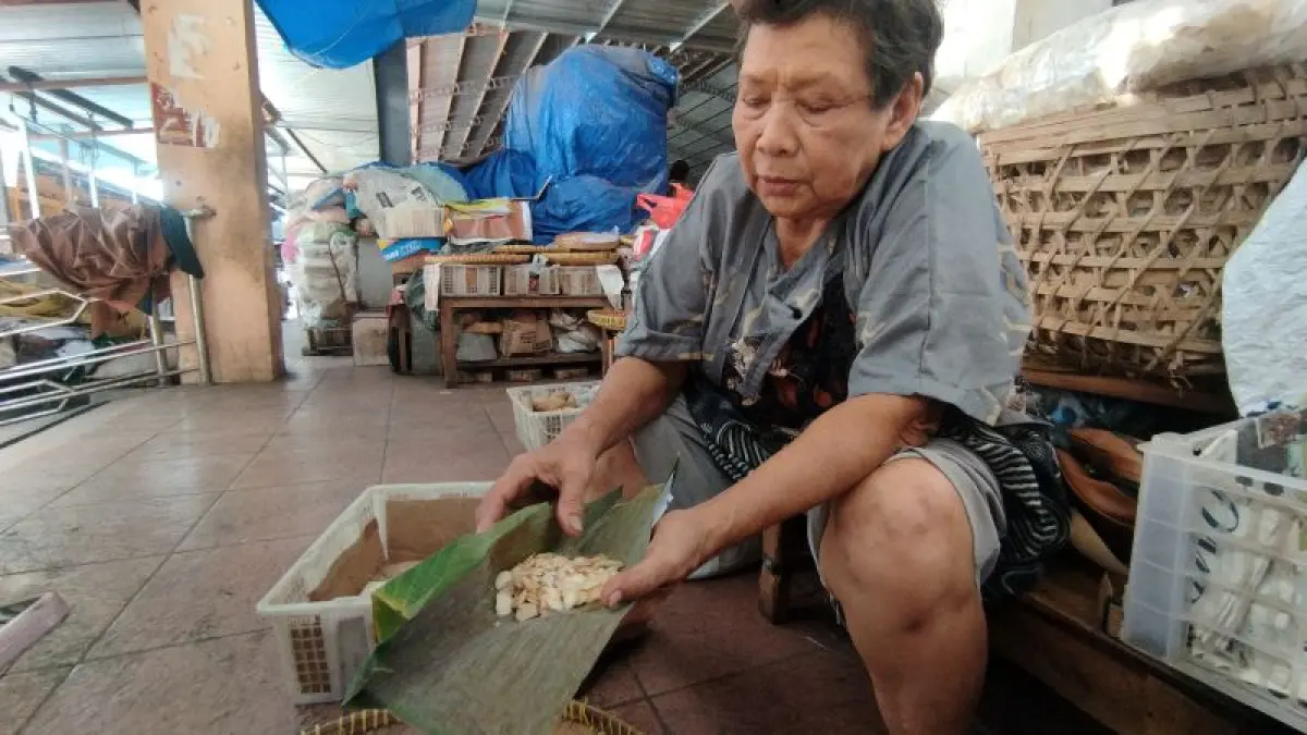 DIKURANGI: Penjual tempe di Pasar Bantul Pujiati sedang memberitahu ukuran tempe yang mengecil setelah harga kedelai impor naik. (Cintia&nbsp;Yuliani/Radar Jogja)