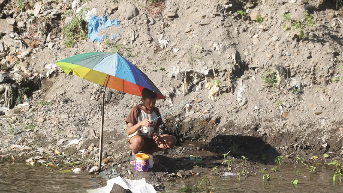Warga menggunakan payung untuk melindungi diri dari sengatan sinar matahari saat memancing di Sungai Winongo, Wirobrajan, Kota Jogja, Senin (6/7/2026). Foto: Guntur Aga Tirtana/Radar Jogja