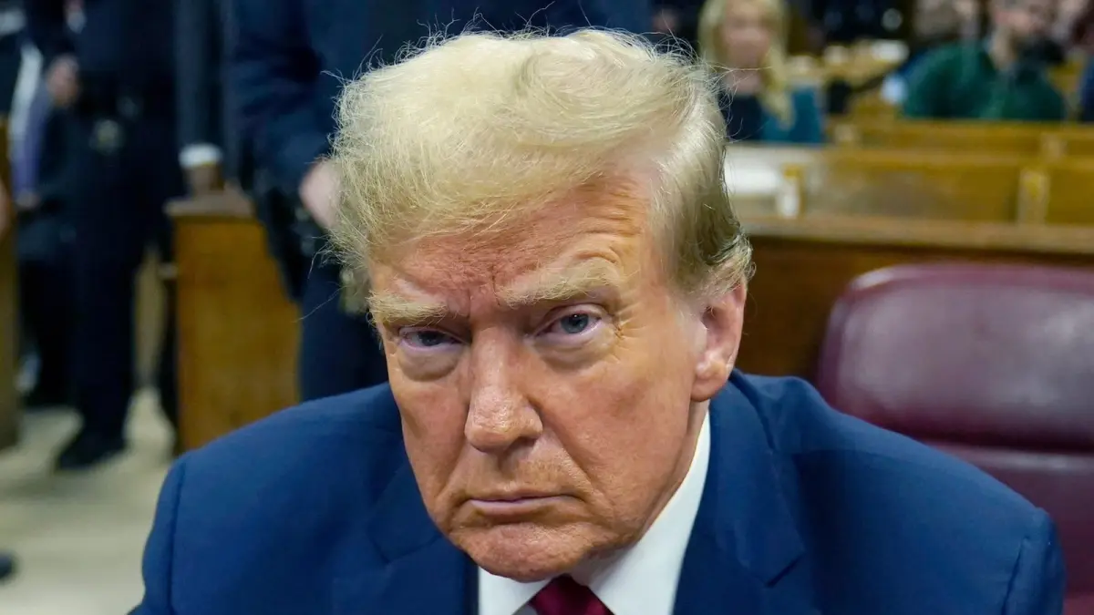 Potret Donald Trump mengenakan jas biru dan pin bendera AS saat menghadiri sebuah sesi persidangan. (X/Politvidchannel)