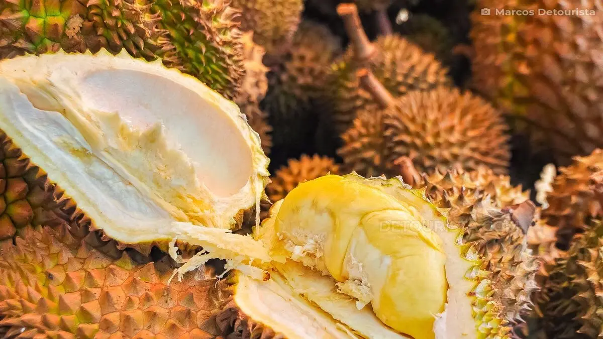Visual detail buah durian yang telah dibelah, memperlihatkan tekstur dan warna daging buah kuning di antara tumpukan buah utuh lainnya. (Pinterest/Detourista)