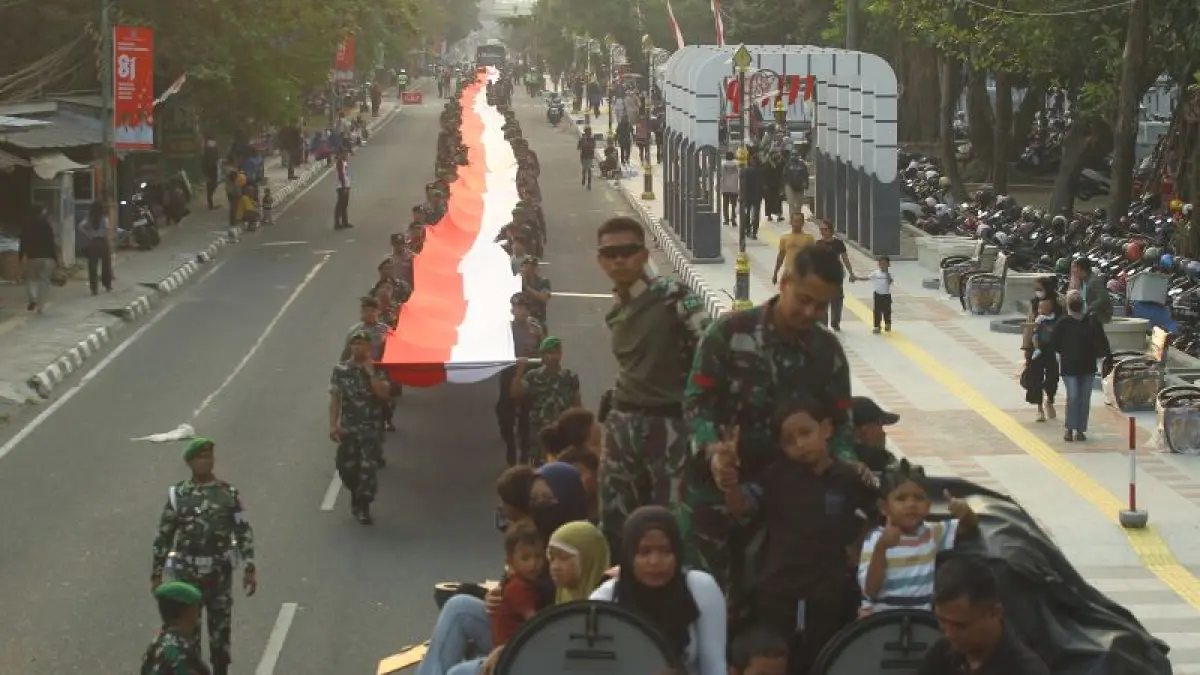 Personel TNI beserta Polisi mengarak bendera merah putih sepanjang 281 meter dan warga menaiki kendaraan militer saat parade Independence Day Military Expo 2026 di kawasan Denggung, Sleman, Jumat (21/8). (Guntur Aga Tirtana/Radar Jogja)
