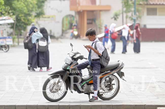 Seorang pelajar SMP bermain gawai di atas kendaraan sepeda motornya seusai mengikuti Masa Orientasi Siswa (MOS) di komplek Masjid Gede Kauman, Jogjakarta, Rabu (20/7). Disdikpora DIJ melarang pelajar SMP mengendarai sepeda motor untuk bersekolah karena be