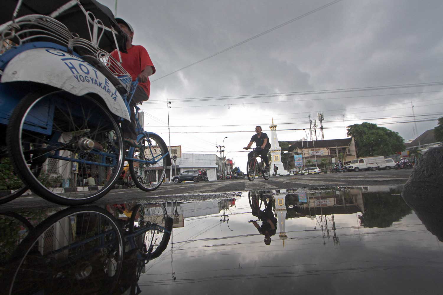SISA HUJAN: Pengayuh becak dan pesepeda melintas di dekat genangan sisa air hujan, di kawasan Tugu Jogja (GUNTUR AGA TIRTANA/RADAR JOGJA)