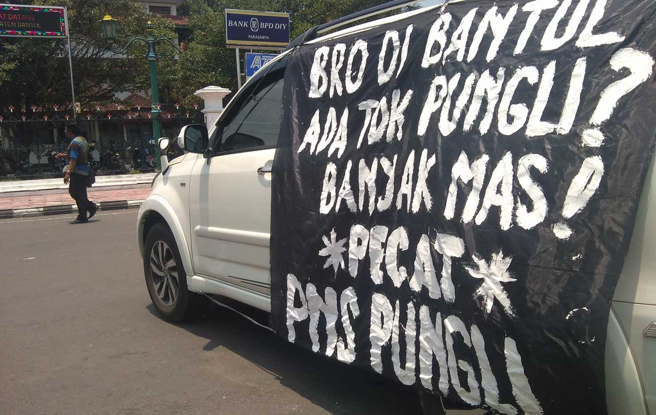 TANPA PAKAI PELICIN: Spanduk tolak pungli yang dibawa pensiunan PNS Satpol PP Bantul Ngadiono saat demo tunggal, kemarin (19/10).(Foto:ZAKKI MUBAROK/RADAR JOGJA)