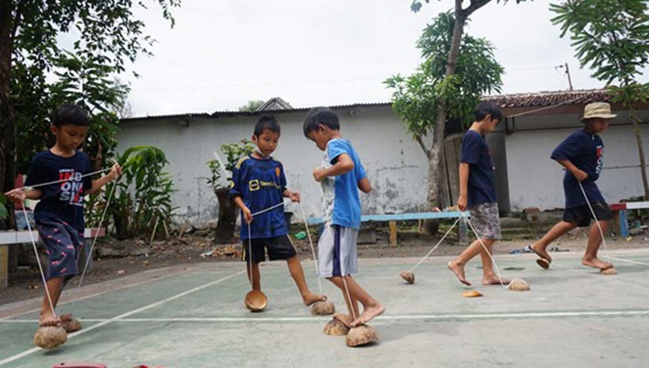 AGAR LESTARI: Mahasiswa KKN UNY mengajarkan permainan tradisional kepada anak-anak di wilayah Giwangan kemarin (5/9). KKN UNY Annur Galeh Pamungkas mewakkli timnya mengedukasikan permainan egrang batok, bakiak, dan lompat tali.(DOKUMENTASI HUMAS UNY)