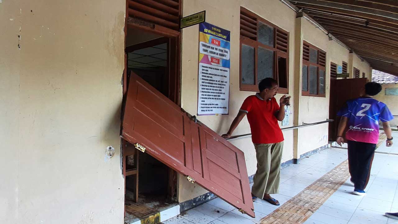 TIDAK LAYAK - Seorang guru olahraga mengangkat pintu yang terlepas di salah satu ruang kelas SD Candibaru Padukuhan Kerdon, Kalurahan Jatiayu, Kalurahan Karangmojo kemarin (21/2).(GUNAWAN/RADAR JOGJA)