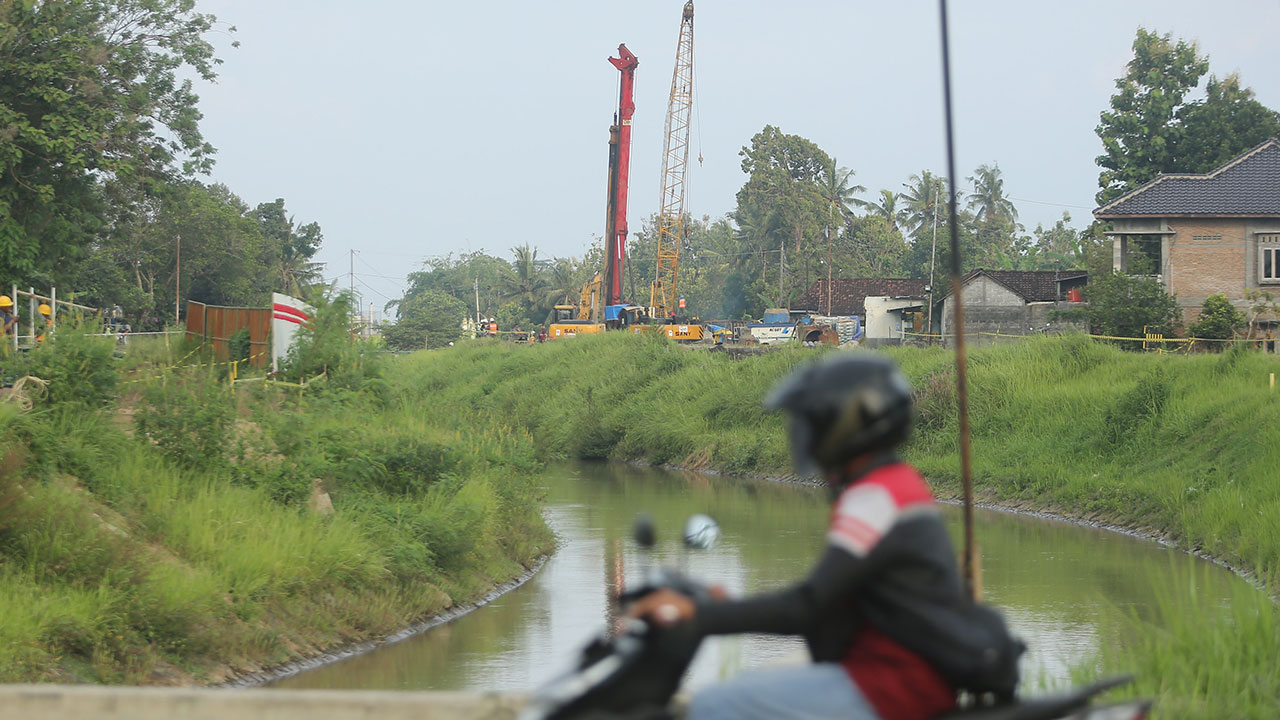 ILUSTRASI: Warga melintas di pinggir Selokan mataram dengan berlatar proyek pembangunan jalan tol di kawasan Margodadi, Sayegan (ELANG KHARISMA DEWANGGA/RADAR JOGJA )