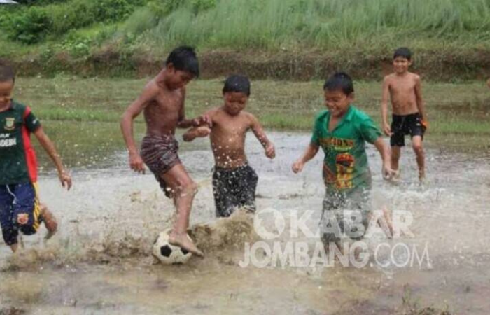 ILUSTRASI : Anak-anak sedang bermain sepak bola ditengah hujan.