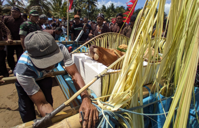 Seorang warga nelayan mengikat tali agar kepala kerbau tidak terjauh saat dibawa ke tengah laut.