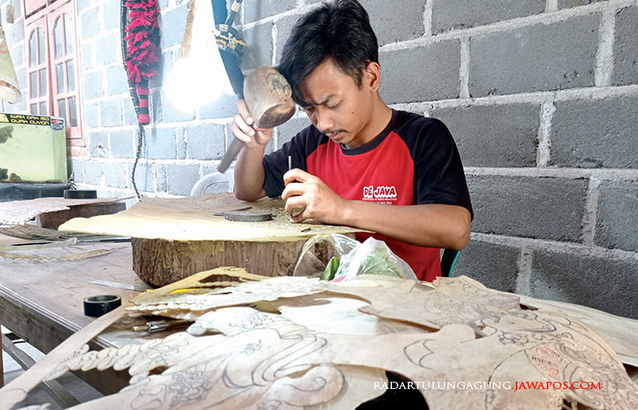 TELITI: Rio memahat lembaran kulit sapi untuk jamang barongan di rumahnya kemarin (30/7).