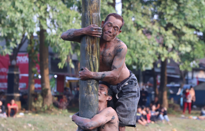 GEMBIRA: Salah satu peserta panjat pinang di Sungai Ngrowo rela belepotan lumpur demi mendapat hadiah di puncak pohon, Minggu (20/08).