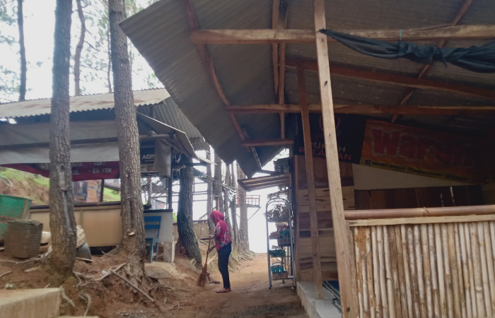 SEPI: Seorang pedagang sedang menyapu dedaunan jatuh agar lingkungan warung tetap bersih.