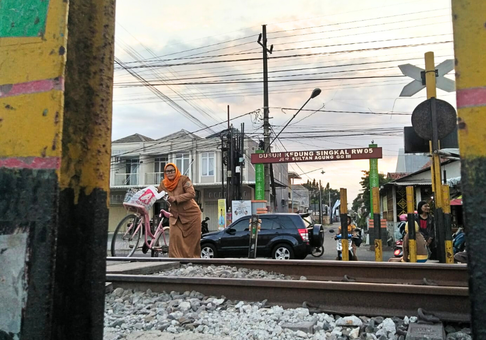 Seorang ASN sedang menuntun sepeda ketika menyeberangi perlintasan KA sebidang tanpa palang pintu di Dusun Kedungsingkal, Desa Ketanon, Kecamatan Kedungwaru, Tulungagung, Senin (8/7/2024).
