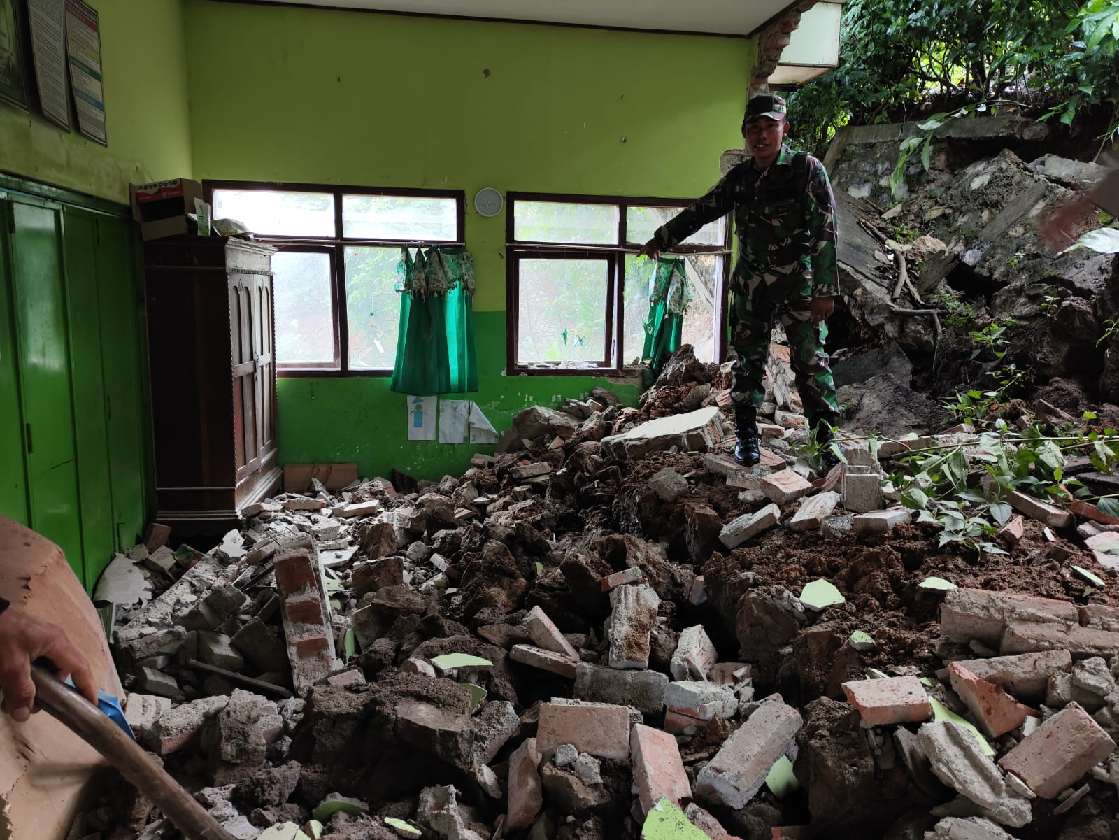 HANCUR: Seorang personel TNI mennunjukkan dinding SDN 5 Ngelebng yang hancur diterjang longsor.
