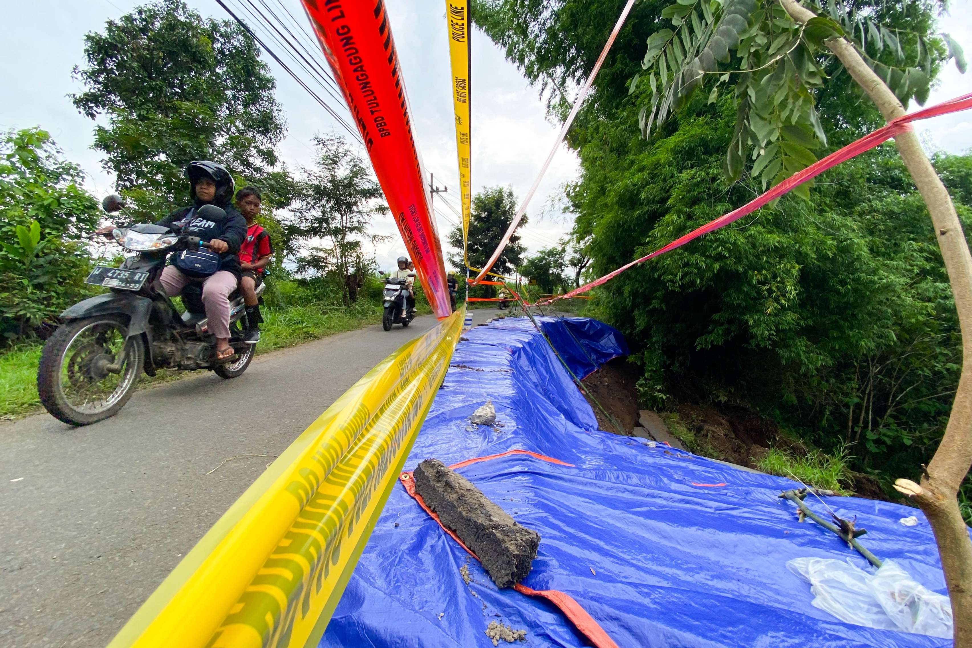 BERGANTIAN: Warga Dusun Mojogitik, Desa Gedangan, Kecamatan Karangrejo menjaga areal jalan yang amblas sepanjang 30 meter kemarin. Saat ini tersisa satu jalur. (DR PERDANA/RADAR TULUNGAGUNG)