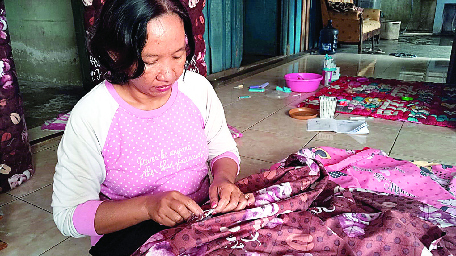 Supraptieni sedang menjahit kain pembungkus kasur kapuk di kediamannya di Desa Sodo, Kecamatan Pakel.