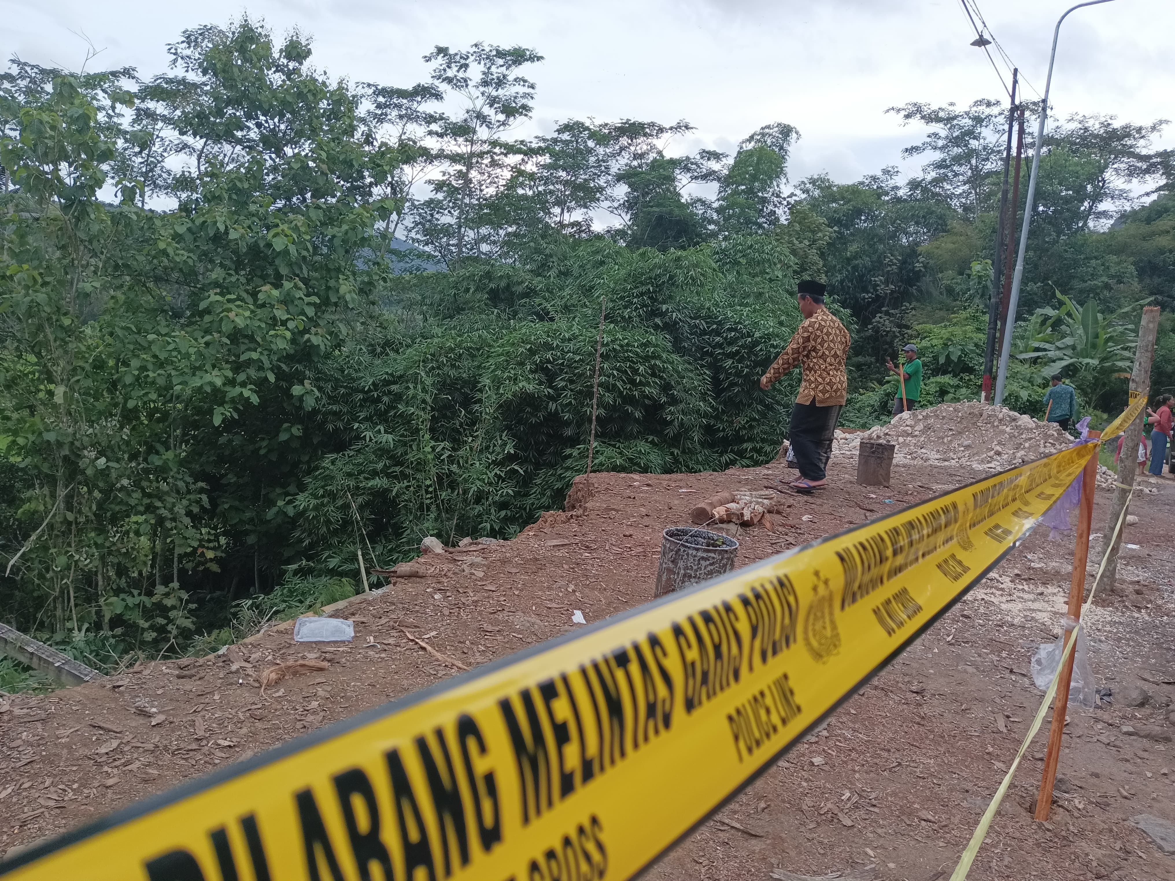 BAHAYA: Seorang warga melewati garis polisi untuk melihat kondisi longsor di Desa Bogoran.