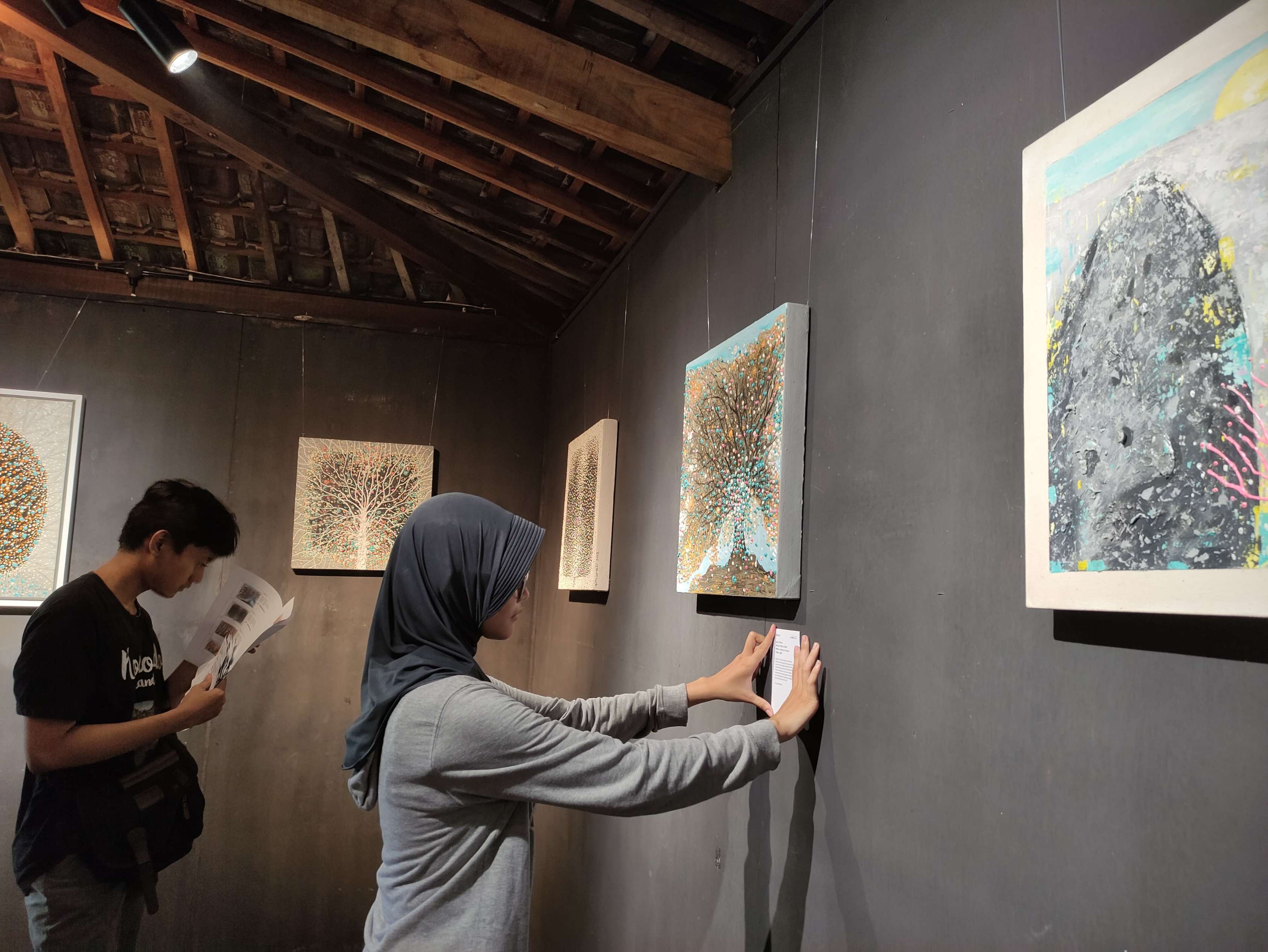Penikmat seni sedang melihat hasil goresan kuas pelukis Tulungagung Nurali dan muridnya Laila Maghfiroh pada Sabtu (15/2) malam. (SANDY YUWANA/RADAR TULUNGAGUNG)