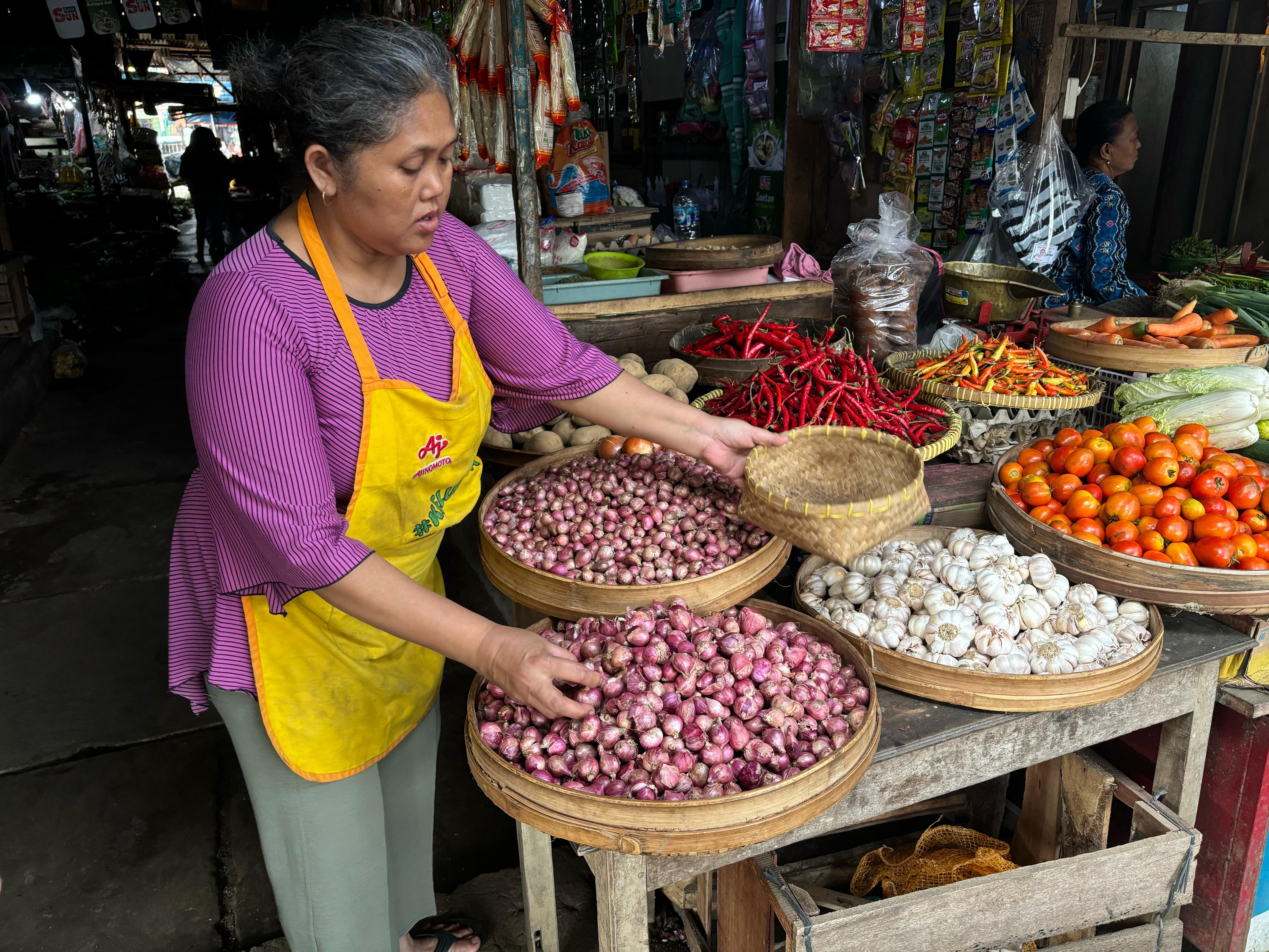 Pedagang dengan telaten melayani pembeli, menyusun bawang merah dan bahan segar lainnya di pasar tradisional.