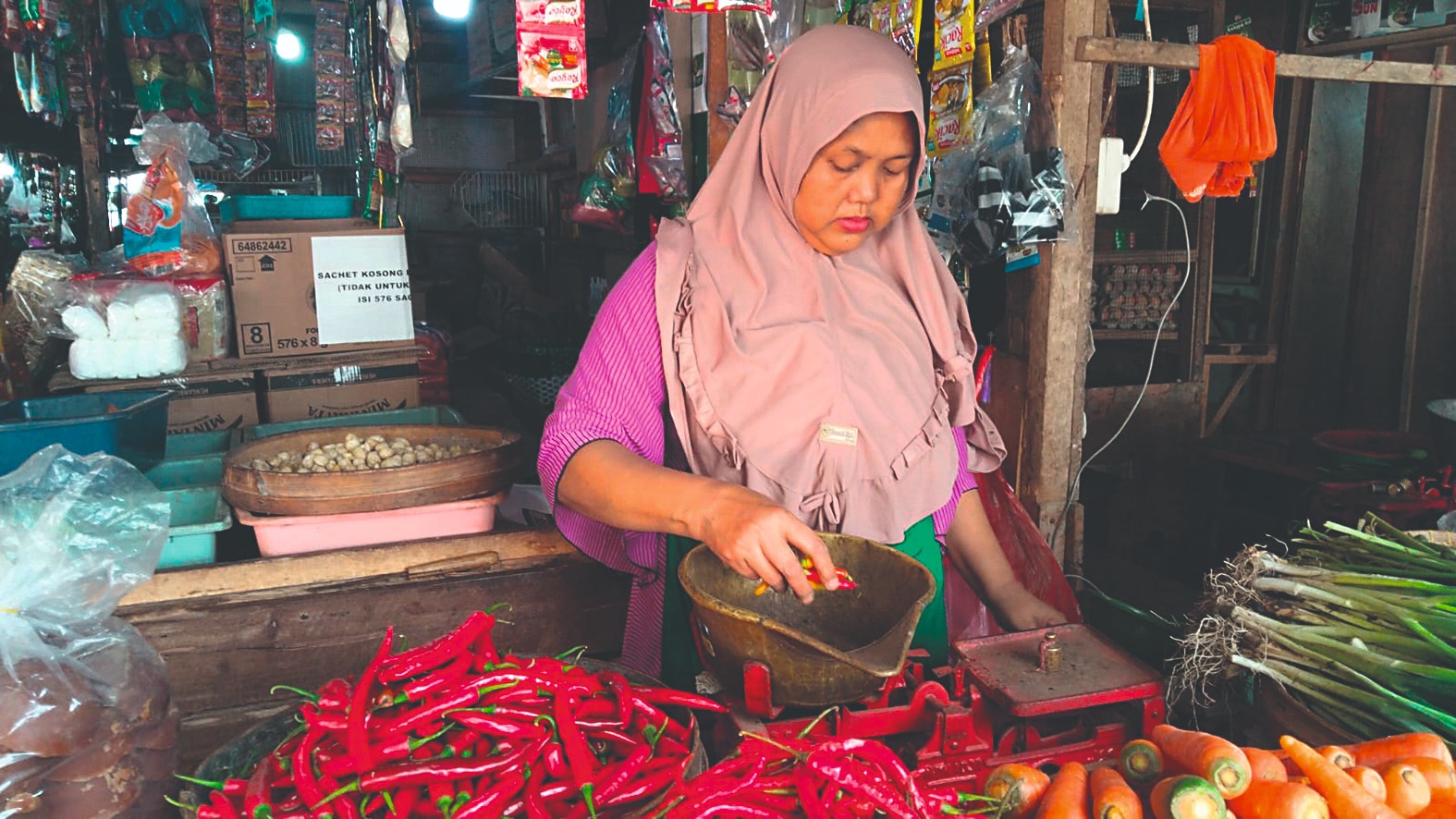 Mariah, salah seorang pedagang sayuran di pasar tradisional, sedang menimbang cabai rawit yang harganya terus menurun