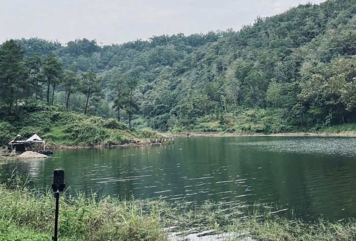 Ilustrasi danau tenang di Tulungagung yang dikelilingi perbukitan hijau, menghadirkan suasana alam yang sejuk dan menenangkan jiwa.
