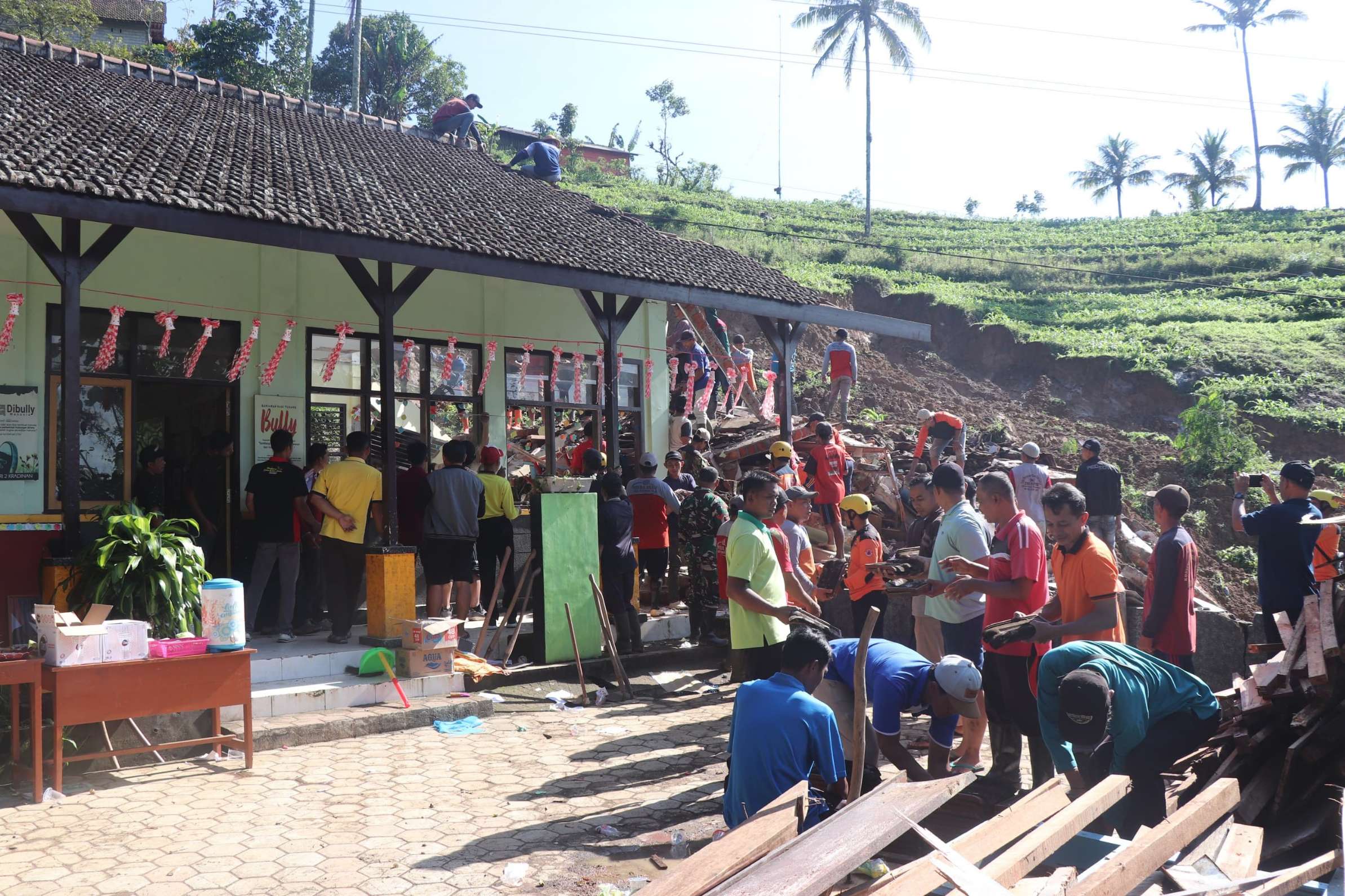 Warga dan personel gabungan bekerja bakti membersihkan SDN 2 Kradinan, Tulungagung yang terdampak longsor. (SANDY YUWANA/RADAR TULUNGAGUNG)