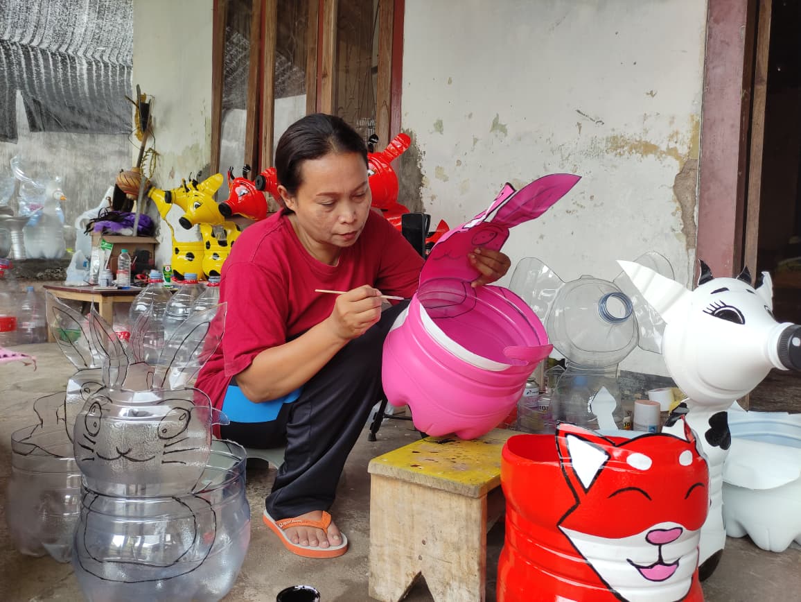 Mimi Hani sedang mewarnai pot karakter yang terbuat dari galon bekas di rumahnya, Senin (12/1). (SANDY YUWANA/RADAR TULUNGAGUNG)