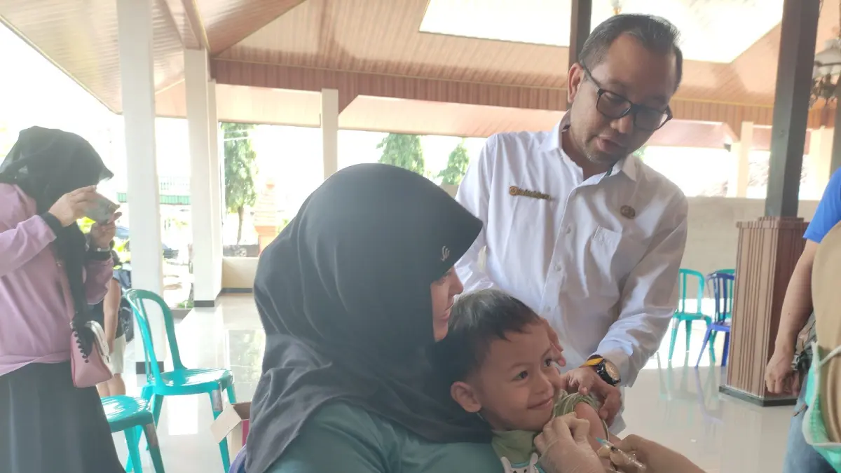 Seorang ibu sedang membawa anak balitanya mendapatkan vaksin ORI Campak di Balai Desa Ringinpitu, Tulungagung, kemarin (1/4).(SANDY YUWANA/RADAR TULUNGAGUNG)