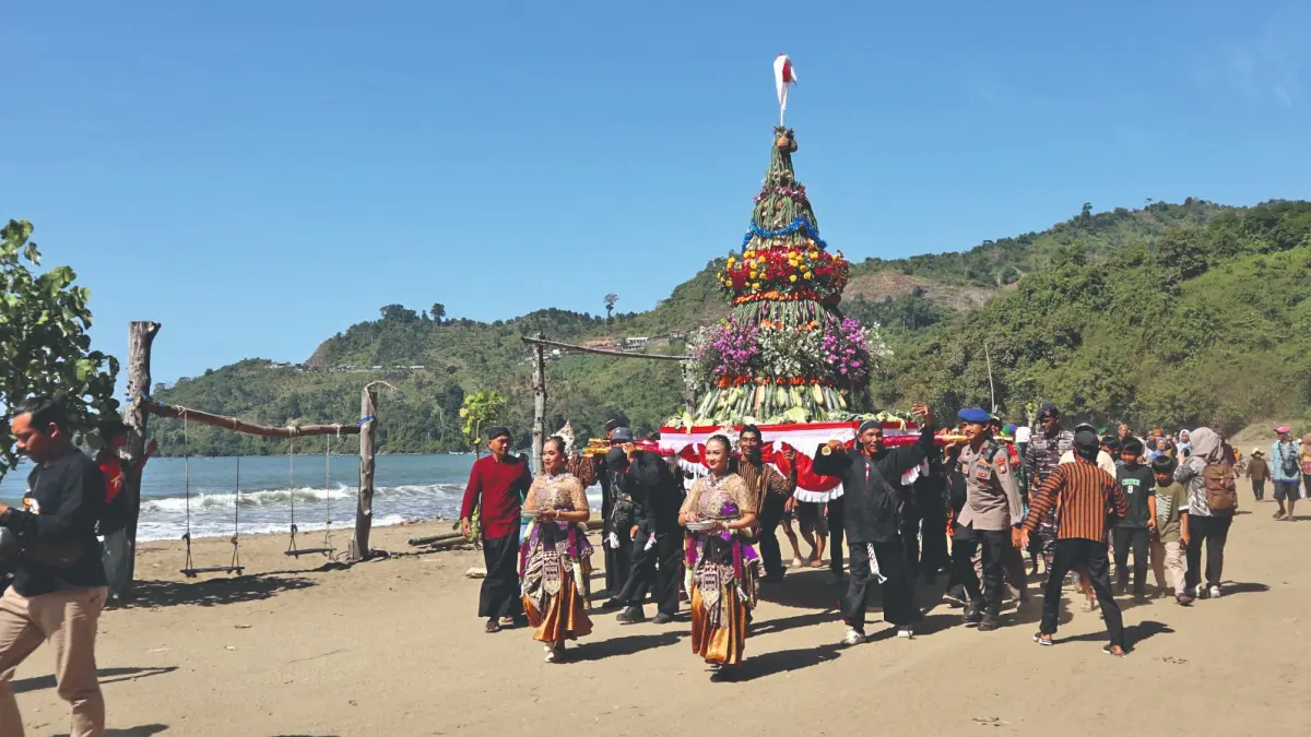 Anggota pokdarwis dan pengunjung menggotong tumpeng besar berisi hasil bumi mengelilingi area Pantai Gemah di agenda Grebeg Sura, Selasa (16/6/2026).(RAHIIQ/RADAR TULUNGAGUNG)