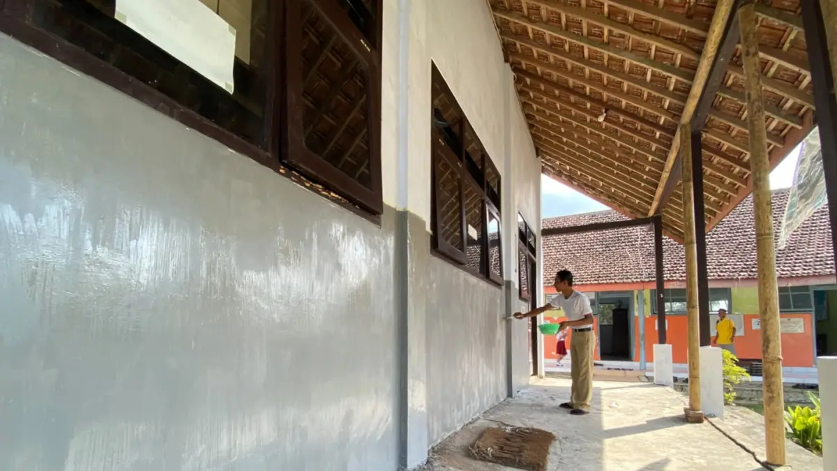 Guru SDN 4 Besuki mengecat tembok ruang kelas yang dibangun pada 2018 silam. (DR PERDANA/RADAR TULUNGAGUNG)