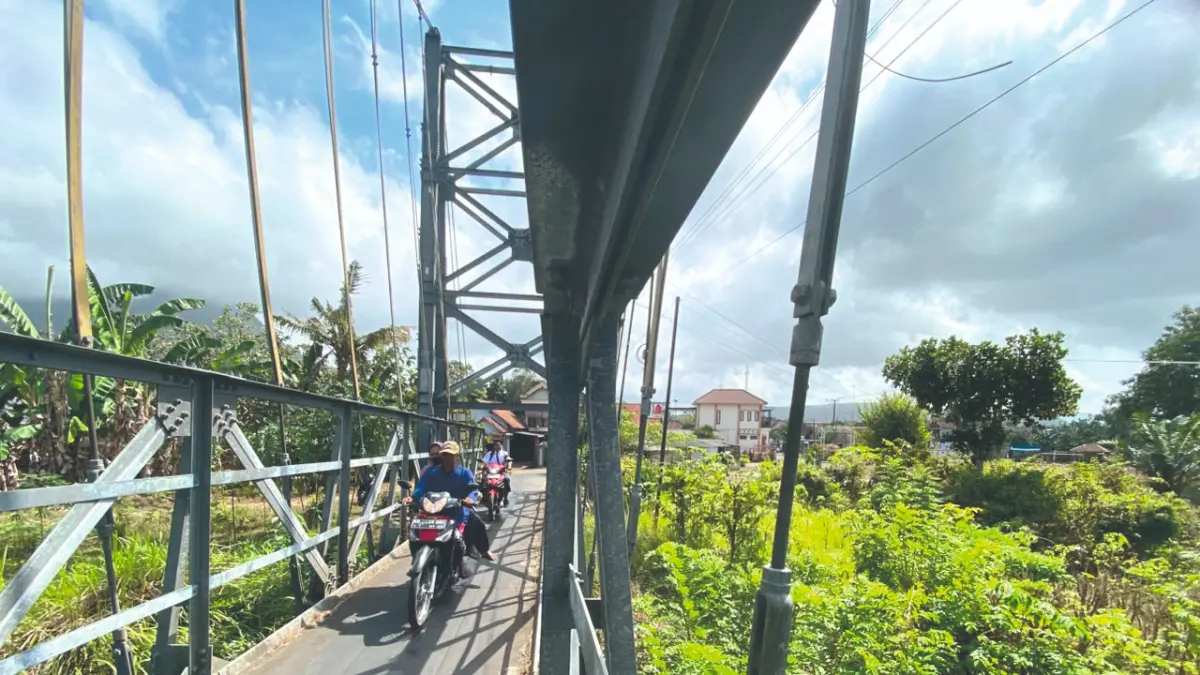 Pengendara sepeda motor melintasi jembatan gantung di Desa Tanggulwelahan, Kecamatan Besuki yang mengangkangi Sungai Parit Raya. Ada area sungai mati di sekitar desa ini yang berubah menjadi pemukiman warga.(DR PERDANA/RADAR TULUNGAGUNG)