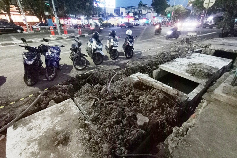 SOLUSI BANJIR: Pengendara kendaraan bermotor melintas tak jauh dari pengerjaan proyek saluran air di Jalan Karangmenjangan, Surabaya, Jumat (14/7). (SURYANTO/RADAR SURABAYA)