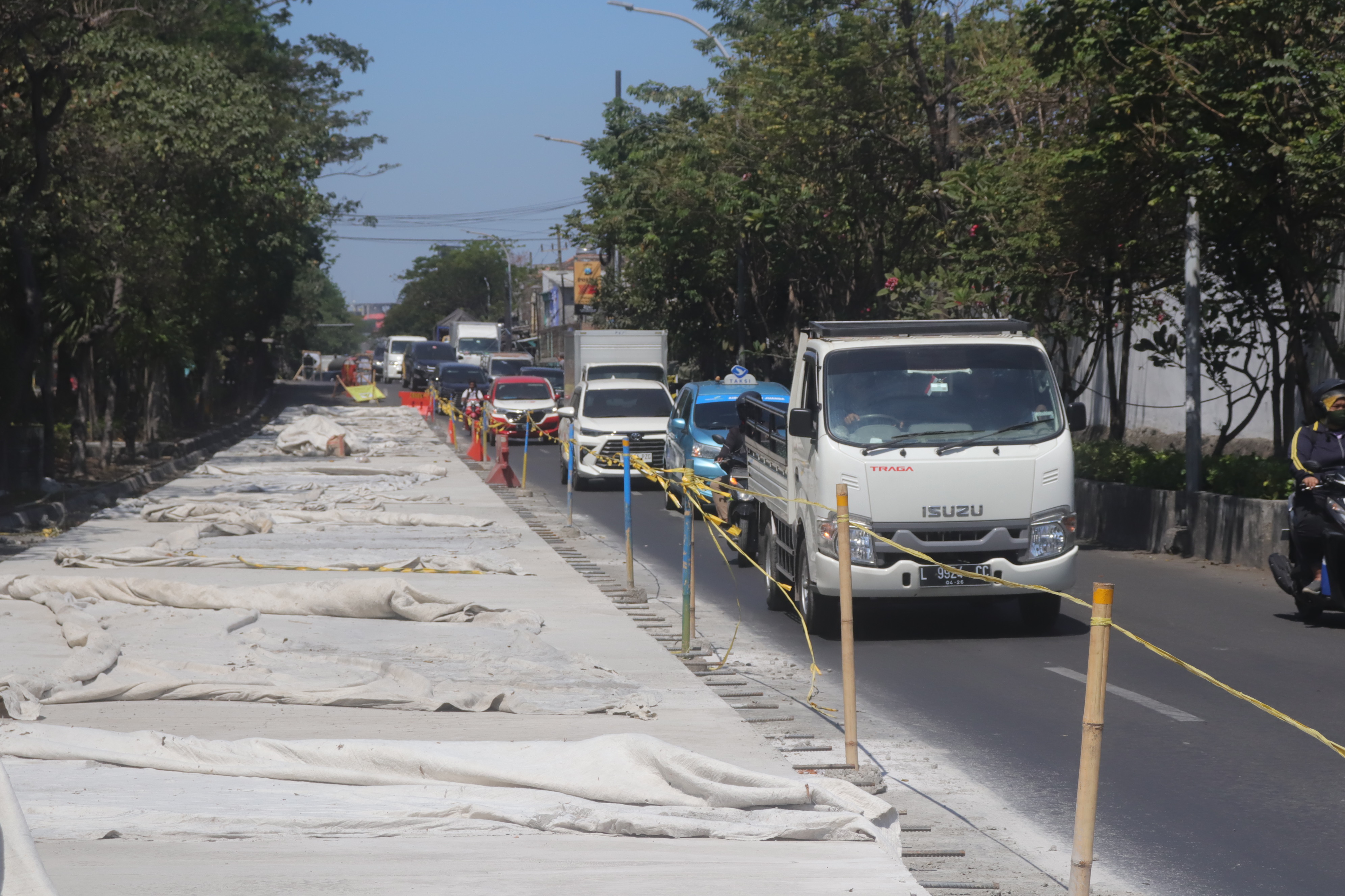 TERUS DIKEBUT: Pengendara kendaraan bermotor melintas tak jauh dari proyek betonisasi Jalan Dupak, Surabaya. (SURYANTO/RADAR SURABAYA)