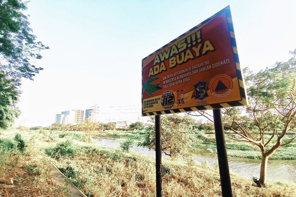 WARNING: Papan imbauan waspada terhadap buaya yang dipasang di semapadan Sungai Jagir di kawasan Nginden, Surabaya. (SURYANTO/RADAR SURABAYA)
