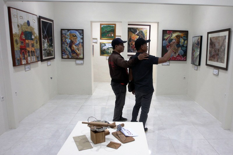 REALITA DI ATAS KANVAS: Pengunjung mengamati lukisan karya sejumlah perupa dalam pameran lukisan bertema Better Cities, Better Lives di galeri di Jalan Sonokembang. (ANDY SATRIA/RADAR SURABAYA)