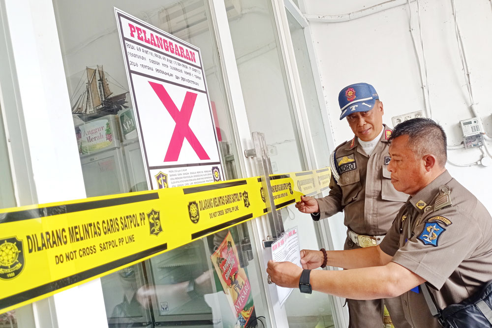 TINDAK TEGAS: Petugas memasang segel di sebuah toko penjual mihol tanpa izin di Gubeng Kertajaya, Surabaya.