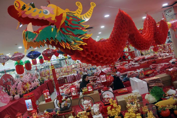 NAGA KAYU: Pegawai di tenan penyedia pernak-pernik Imlek di Pasar Atom Mall Surabaya, memasang aksesoris Naga untuk menyambut perayaan Tahun Baru Imlek 2024, Rabu (24/1). (ANDY S/RADAR SURABAYA)