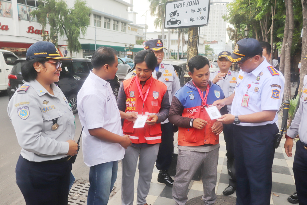 MULAI DICOBA: Petugas Dinas Perhubungan (Dishub) Surabaya membagikan kode QRIS kepada jukir di Jalan Tunjungan, Surabaya, Kamis (1/2).