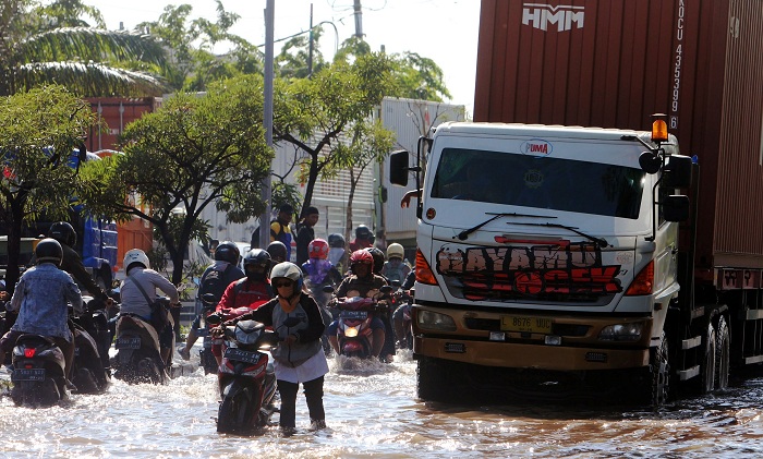 TERPUTUS: Pemotor nekat menerobos banjir yang menggenangi kawasan jalan Tambak Oso Wilangun Surabaya, meskipun ada beberapa yang mendorong motornya karena mogok, Selasa (6/2). (ANDY S/RADAR SURABAYA)