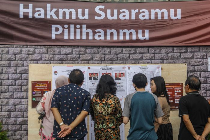 CEK DAN RICEK: Warga Rungkut Surabaya membaca seputar informasi Pileg 2024 saat pemungutan suara pada Februari lalu. (SURYANTO/RADAR SURABAYA)