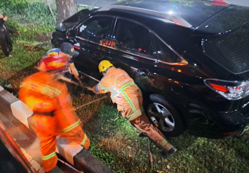 LAKA TUNGGAL: Petugas DPKP Surabaya melalukan evakuasi mobil yang naik ke taman dan menabrak pohon di Jalan HR Muhammad Surabaya, Jumat (14/6).
