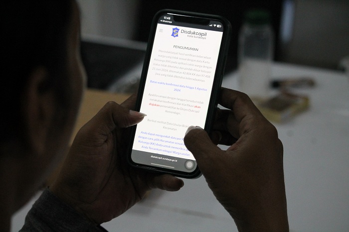 KEPO: Salah satu warga Kota Surabaya melihat pengumuman pemblokiran data KTP melalui gawainya, Minggu (30/6). (SURYANTO/RADAR SURABAYA)