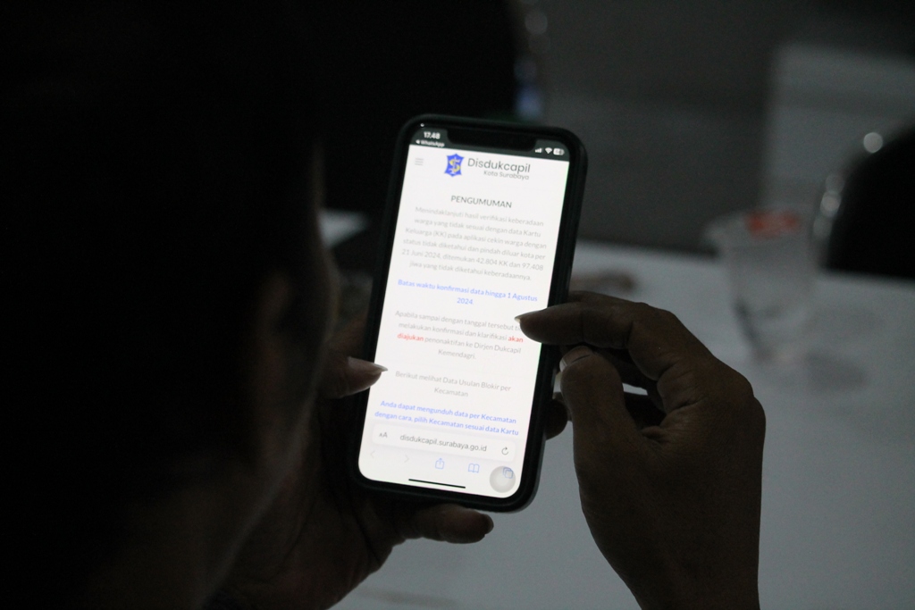Warga melihat pengumuman pemblokiran data KTP melalui gawainya di Surabaya. (SURYANTO/RADAR SURABAYA)