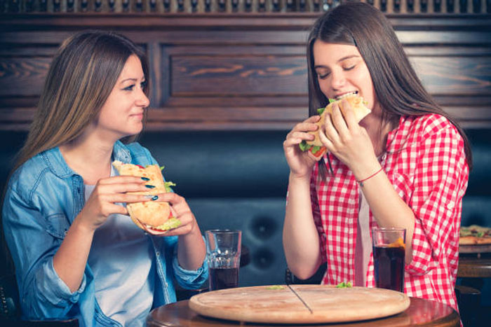 Ilustrasi perempuan menyantap fast food.
